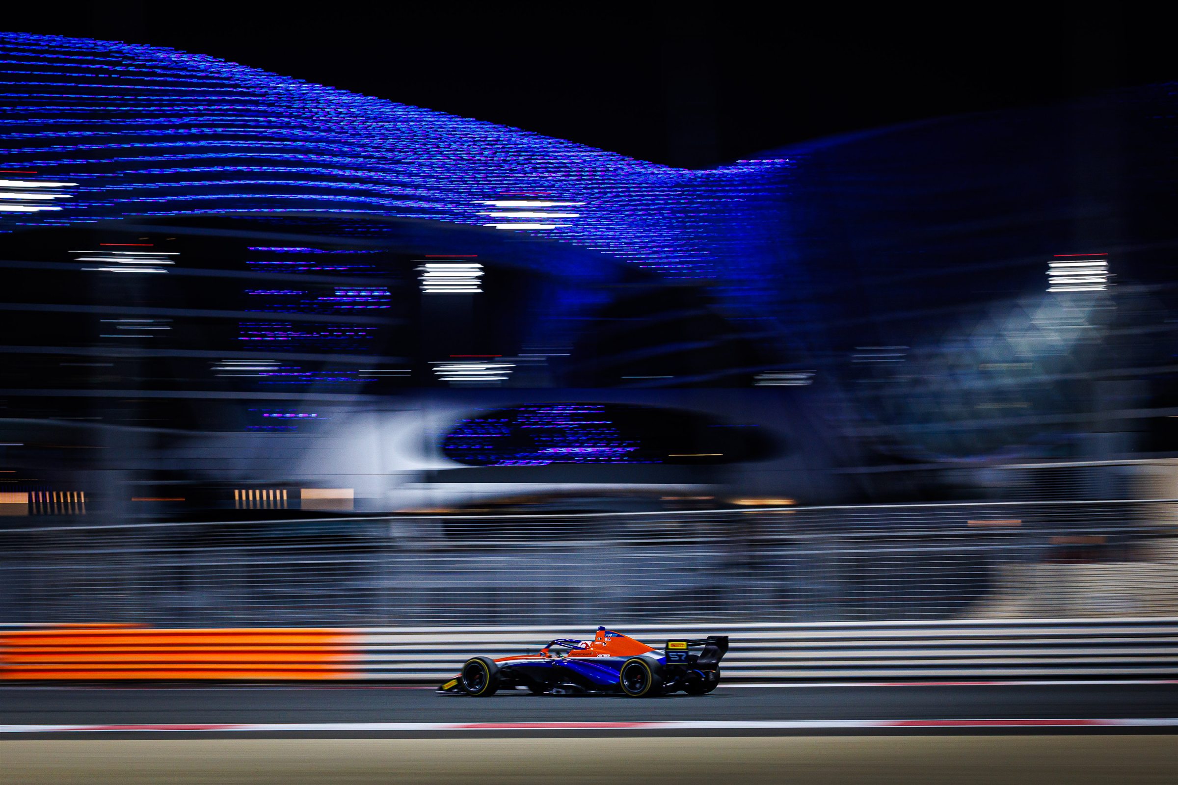 A Racecraft athlete's race car streaking past the illuminated Yas Marina Circuit canopy at night