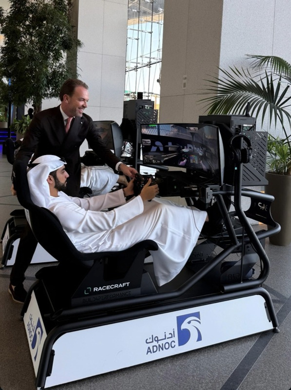 A Racecraft team member guiding a guest in traditional Emirati dress through a simulator session, branded for ADNOC
