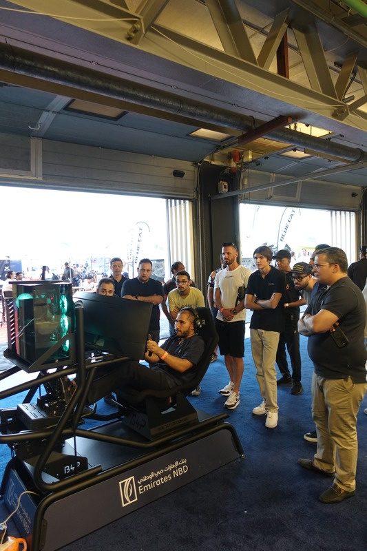 A crowd of onlookers gathered around a guest racing on a Racecraft simulator rig, branded for Emirates NBD